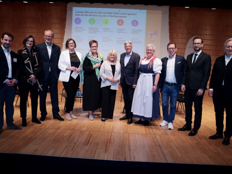 Personen im Halbkreis auf der Bühne, vli.: Sebastian Lücke, Brigitte Winkler-Komar, Klaus Ehrenbrandtner, Julia Schuster, Astrid Legner, Gerda Sandriesser, LH Peter Kaiser, Hanna Wiedenig, Martin Weberhofer, LR Sebastian Schuschnig, Michael Springer