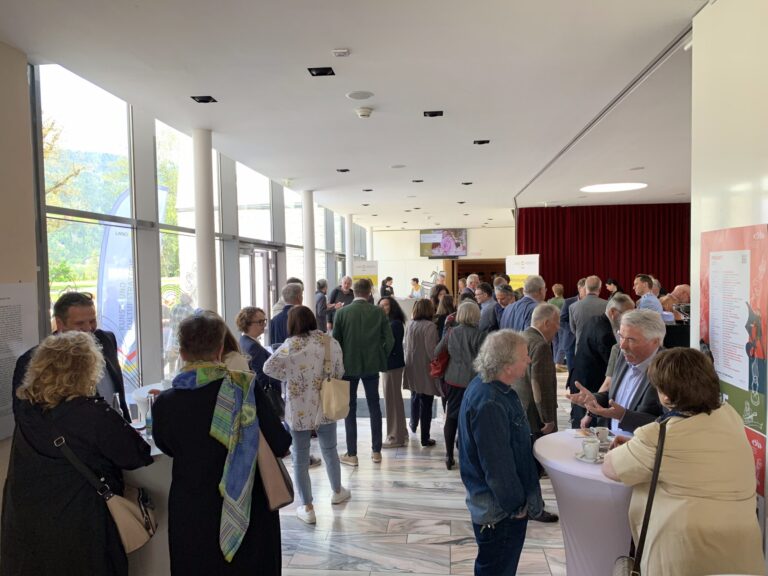 Teilnehmenden stehen an Stehtischen in einem hellen Foyer.